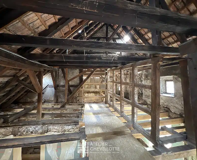 Charpente traditionnelle en bois massif d’un bâtiment à colombages, vue intérieure d’un grenier en cours de restauration avec plancher partiellement refait.