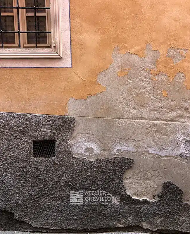 Enduit coloré à la chaux et soubassement enduit à la chaux, fortement dégradés par l’humidité : salpêtre, cloques et pertes de matière.