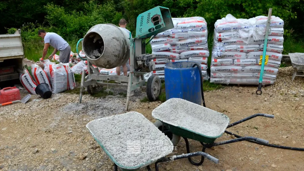 Deux artisans préparent un mélange à la bétonnière sur un chantier, entourés de sacs « Laterlite Plus » destinés à la réalisation d'une dalle de chaux d’un bâti ancien.