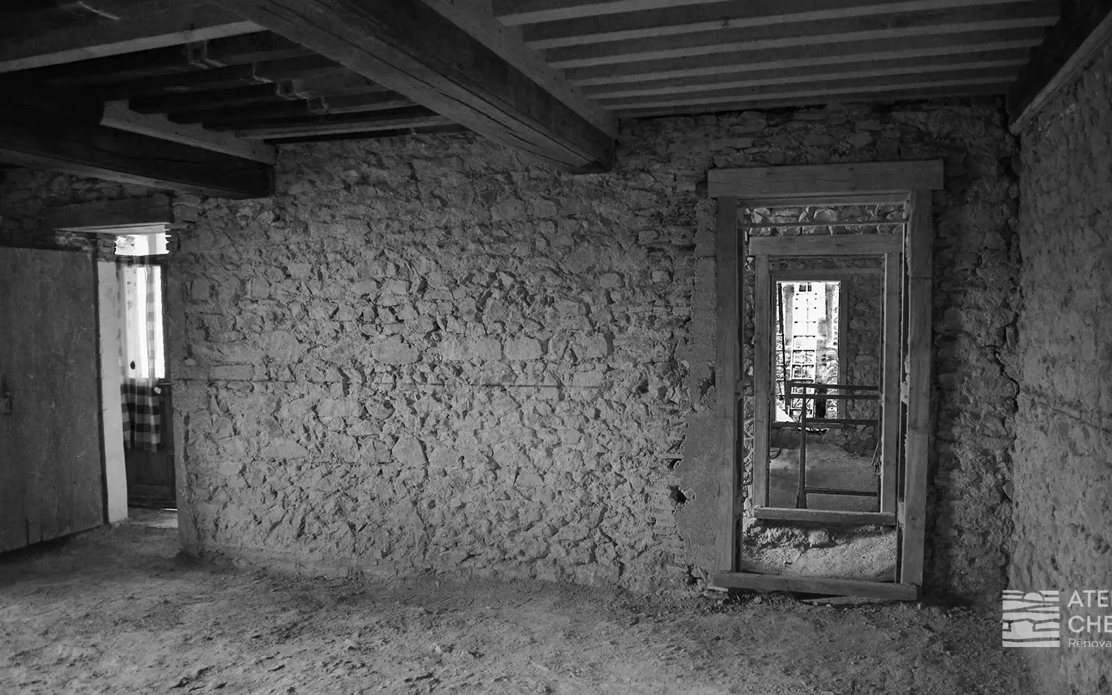 Intérieur avant travaux du bâti ancien avant réhabilitation, montrant des murs en pierre apparente non restaurés, un sol en terre battue et une porte en bois vétuste, révélant le potentiel d’un bâti ancien en attente de restauration.
