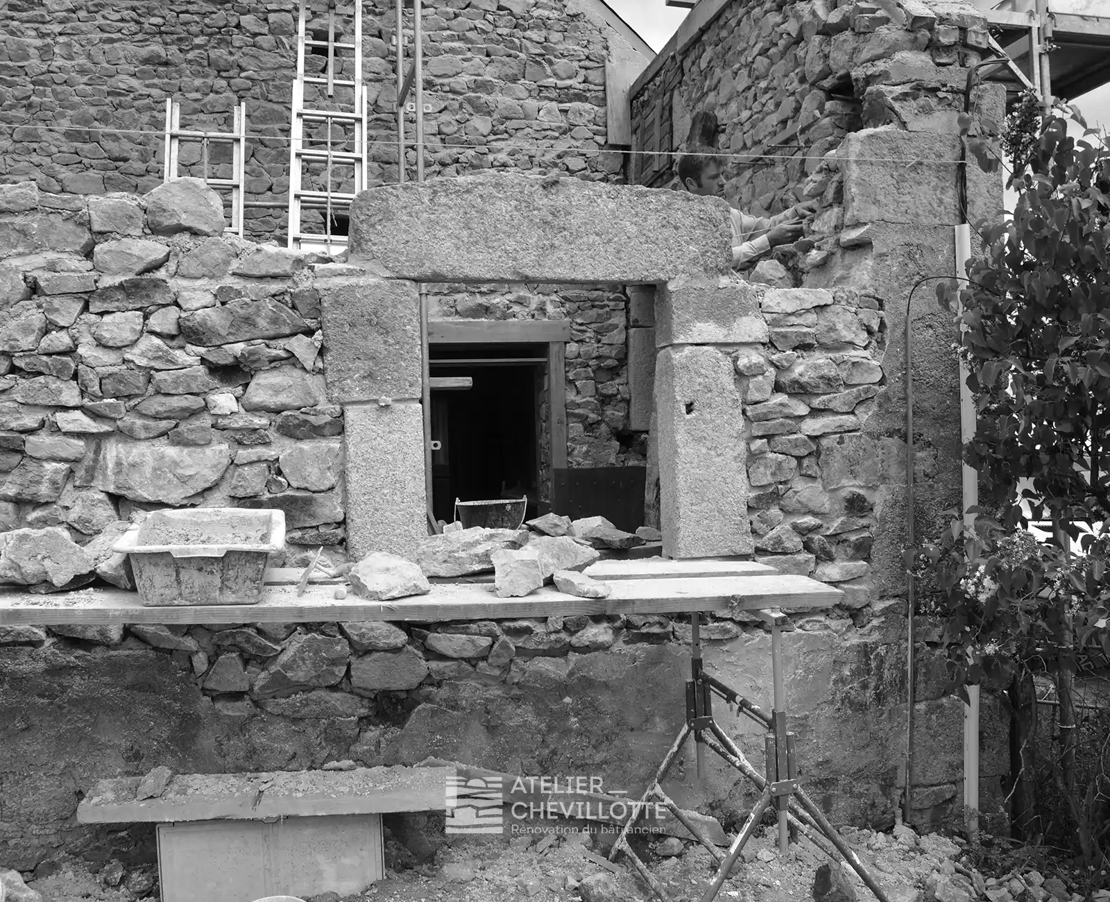 Un artisan qualifié restaure un mur porteur en pierre avec divers outils et blocs sur un échafaudage, illustrant le savoir-faire nécessaire à la maçonnerie de murs anciens.